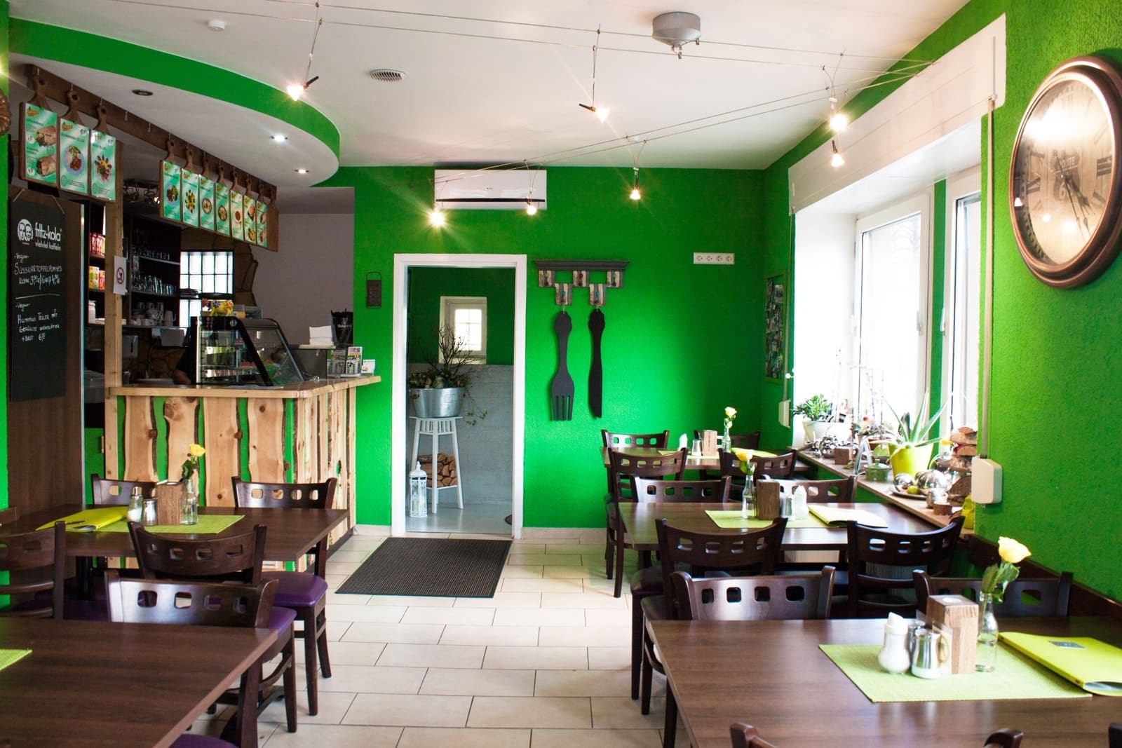 Blick in den Gastraum von Falafel Beirut mit grüner Wand und Holztischen